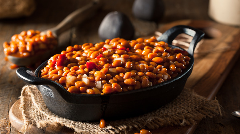a skillet full of homemade barbecue baked beans sits on a wooden table