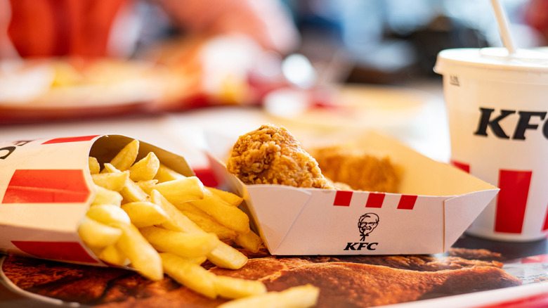 A meal from KFC rests in a tray, consisting of fries, fried chicken, and a small drink