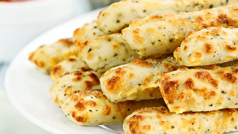 A big white plate of herby, cheese filled breadsticks