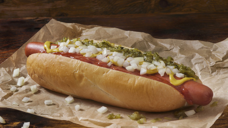 A footlong hot dog is topped with relish, yellow mustard, and raw white onions