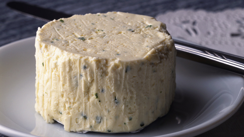 An unwrapped Boursin herbed cheese sits on a plate next to a butter knife