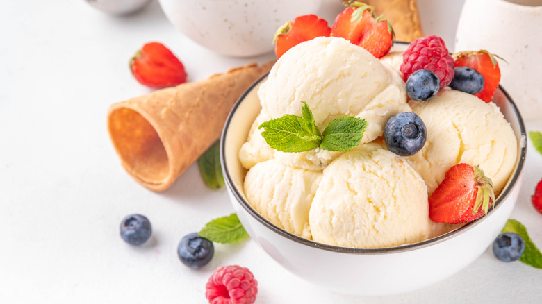 Bowl of vanilla ice cream covered in berries, an empty cone beside it
