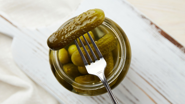 A pickle is selected with a plastic fork out of a jar of small, dill pickles