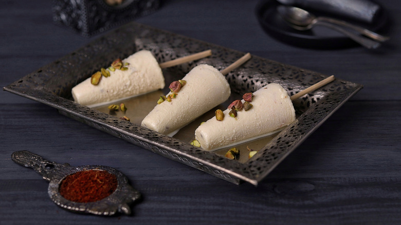 Three kulfi on a plate with pistachio garnish