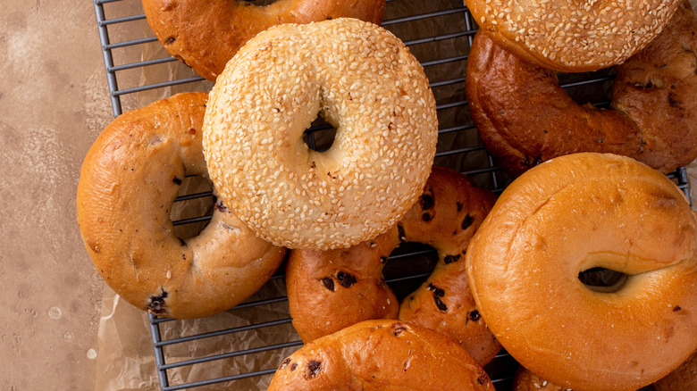 Assortment of bagels to the right on a cooling rack and texturized table.