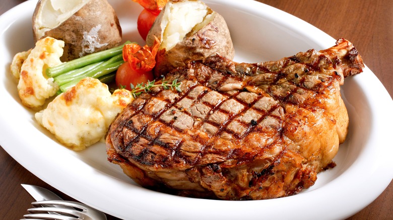 Plate of seared steak with baked potato, mashed potato, green beans and tomato