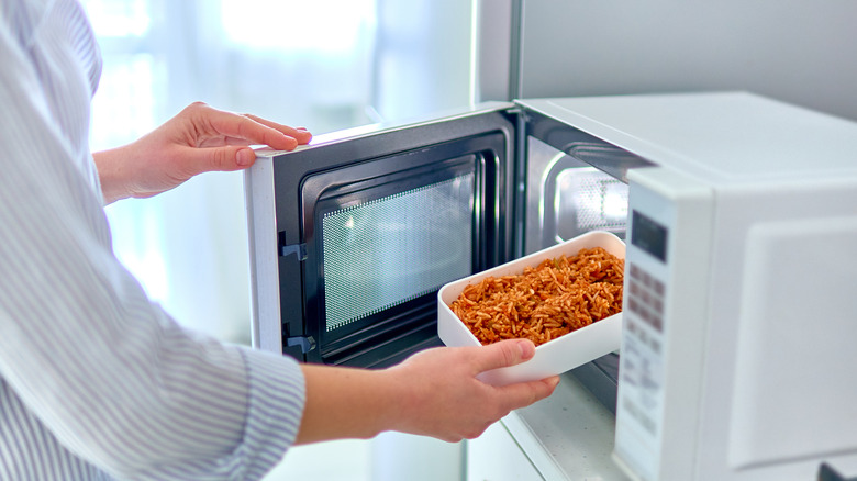 A dish with sauce being placed in a microwave
