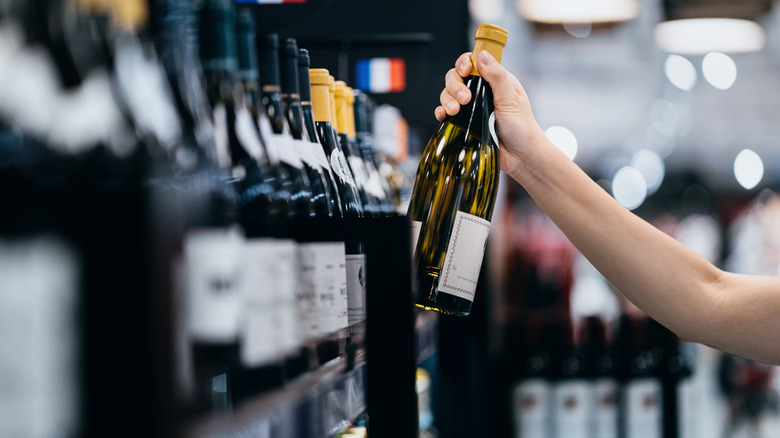 A female hand reaches for a bottle of white wine at a supermarket
