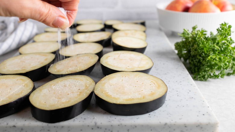 A hand sprinkling salt over eggplant slices